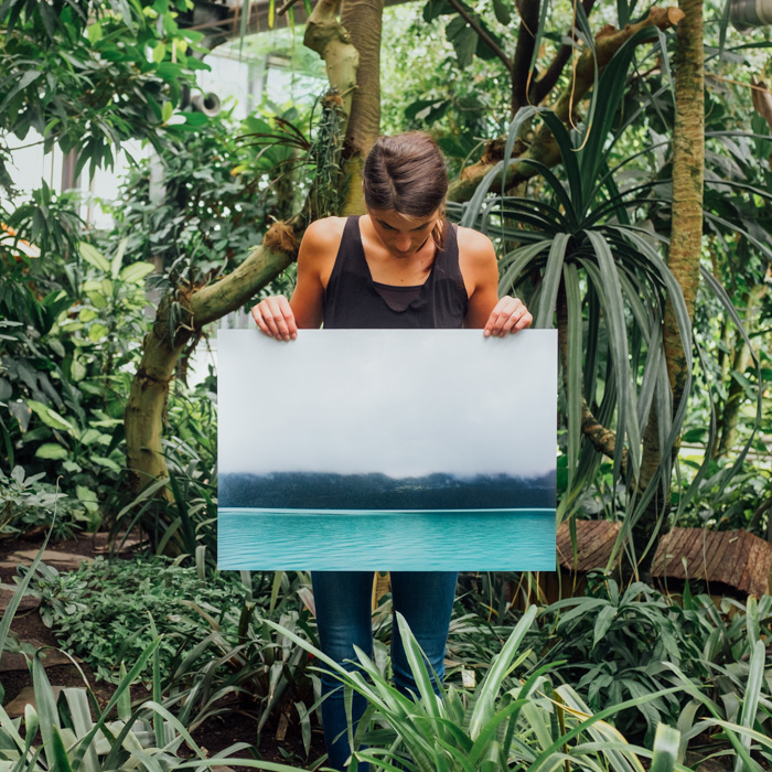 A man standing in a tropical forest setting holding up a large sized photo printing paper 