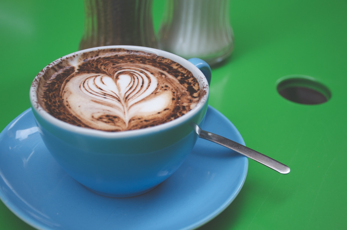 Close up photo of a cappuccino in a blue coffee cup on green background demonstrating color contrast images