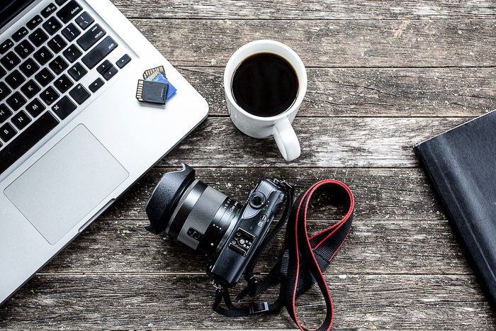 Flat lay of a photographers desk featuring laptop, DSLR camera, coffee cup 