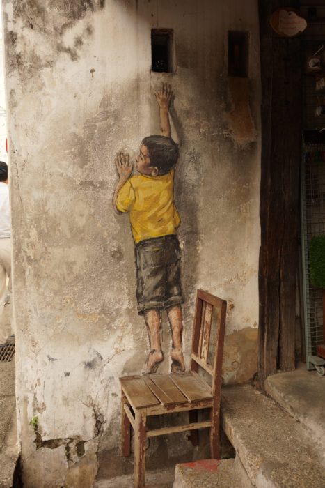 Painting of a boy on a wall with a chair under his feet