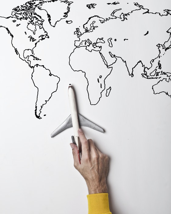 A hand holding a model airplane on a handdrawn map of the world