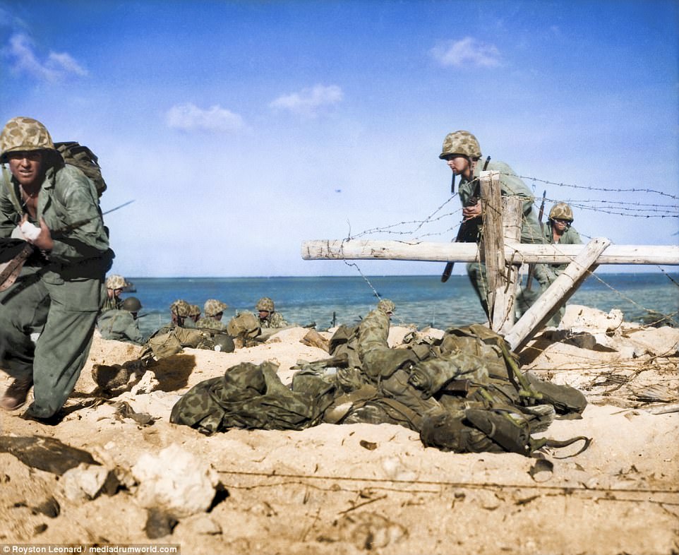 A group of fighters, led by a Marine with a wounded hand, charging from the shore around opened barbed-wire entanglement to battle firmly entrenched Japanese in pillboxes on Tarawa. The photos were restored by colouriser Royston Leonard, from Cardiff