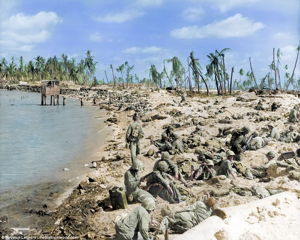 Cpl Robert E Voorhees standing while carrying supplies during the Battle of Tarawa at Red Beach, Bieto, Tarawa. A number of other US troops lay on the beach as others sit and chat. The images were published today to mark the anniversary of the America